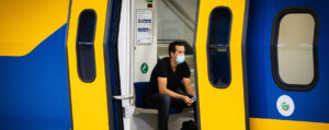 Op deze foto zie je een man in trein met een mondkapje