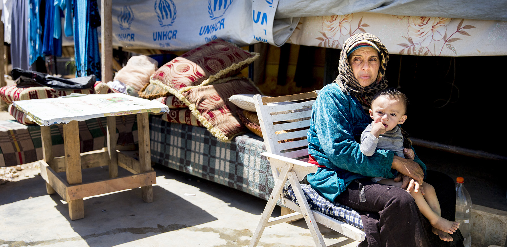 Op deze foto zie je een Syrische vluchtelinge met haar kind op schoot voor een tent.