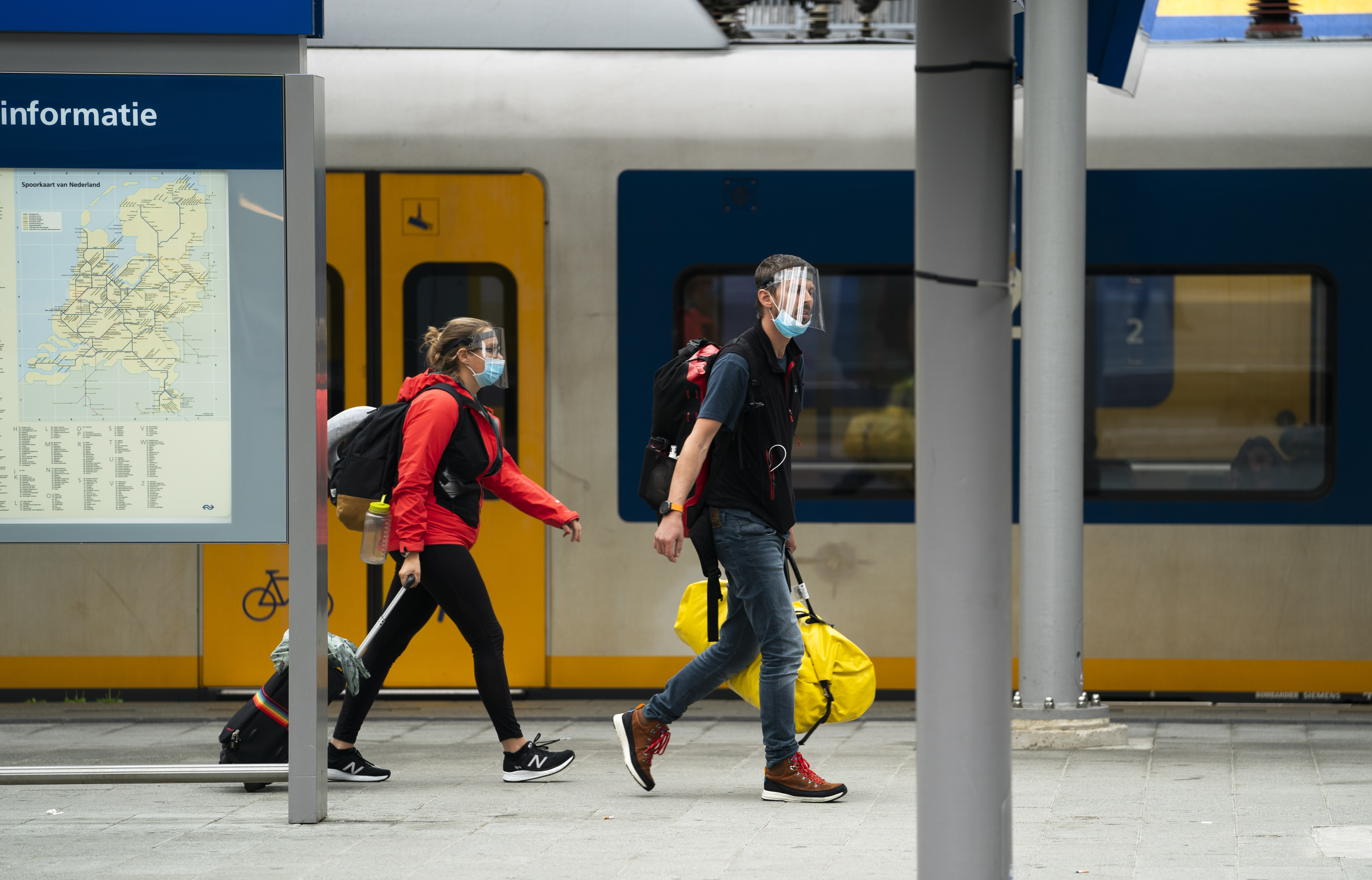 Een foto van twee reizigers op het perron van een treinstation