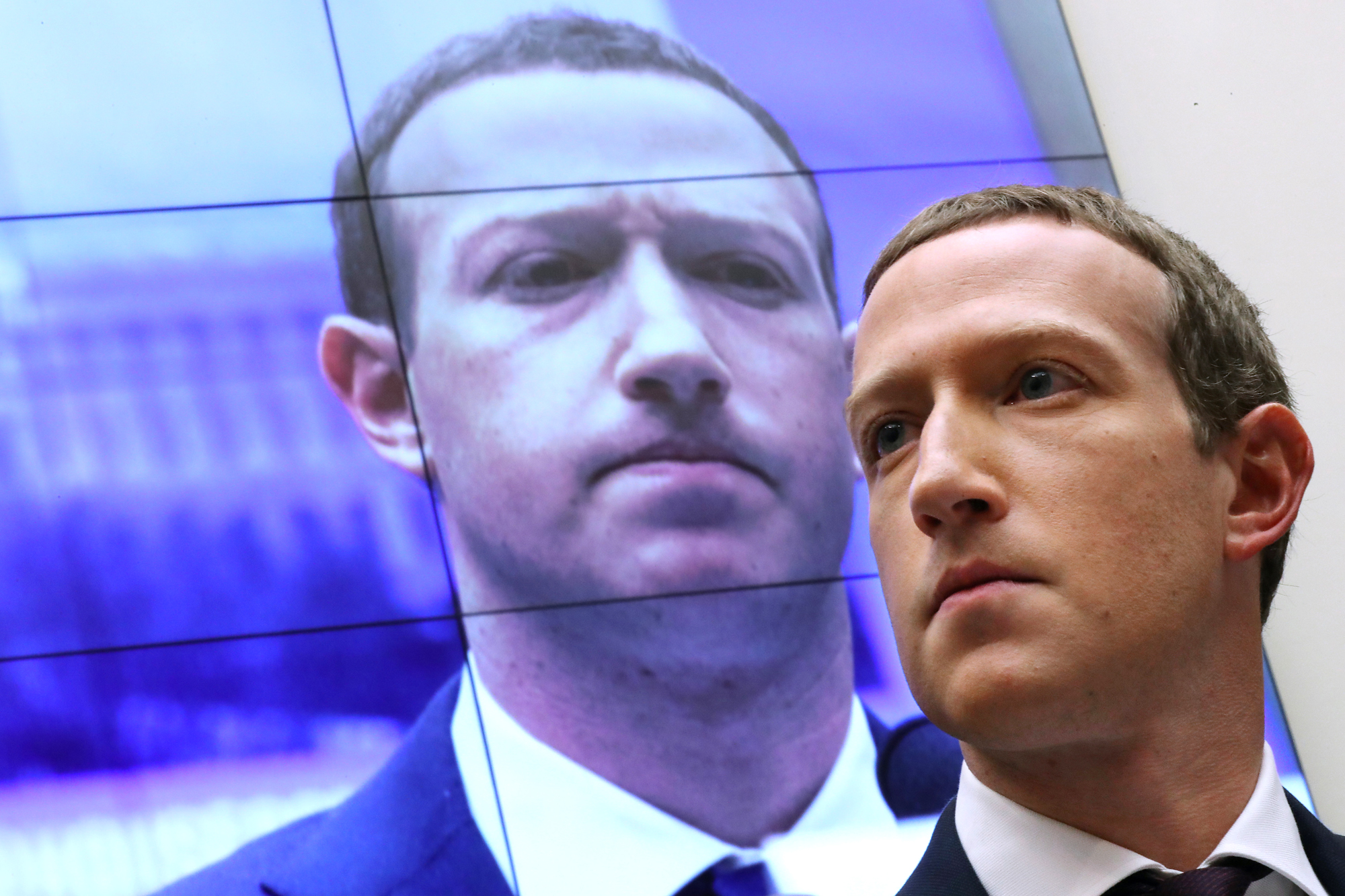 Een foto van Facebook CEO Mark Zuckerberg met achter hem een scherm waarop zijn gezicht geprojecteerd wordt