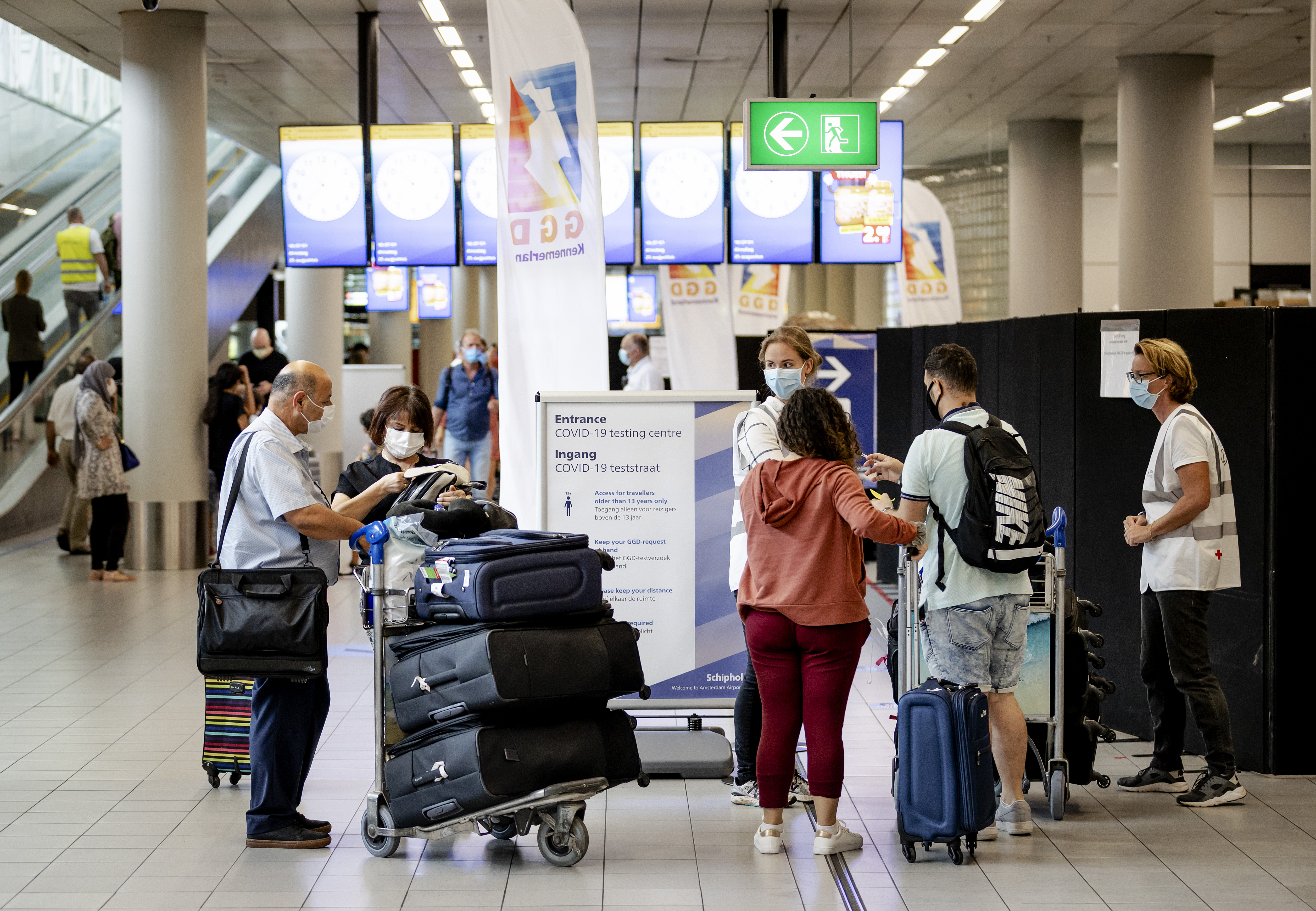 Op deze foto zijn reizigers op Schiphol te zien, met koffers en een mondkapje op.