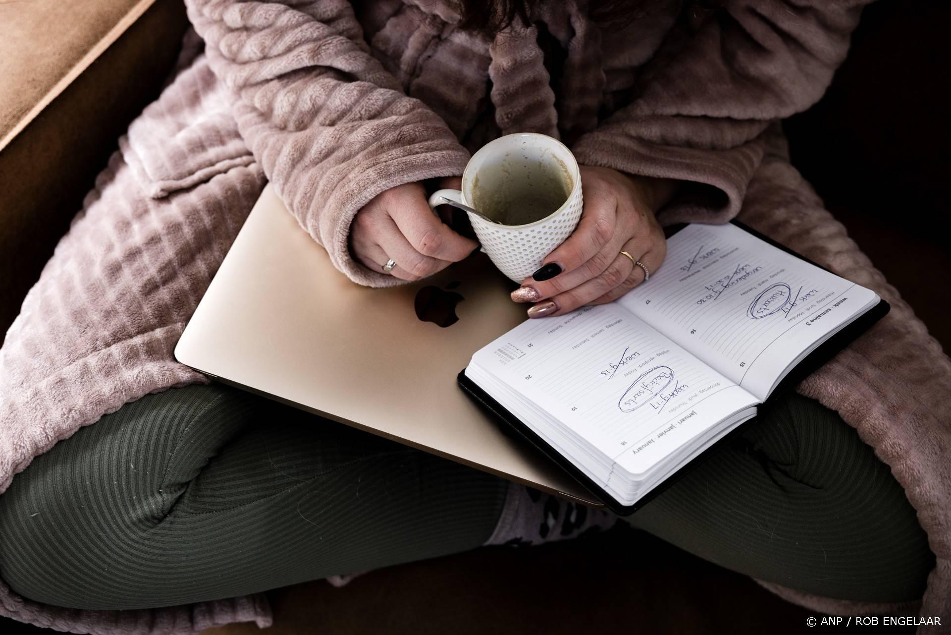 ILLUSTRATIEF - Een vrouw in ochtendjas met gesloten laptop, agenda met geschrapte werkdagen en een lege kop koffie op de bank. ANP ROB ENGELAAR